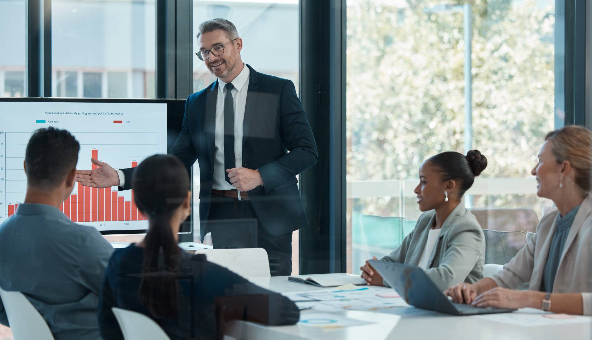 Man in a boardroom in front of other women and men. He is coaching the executive team.